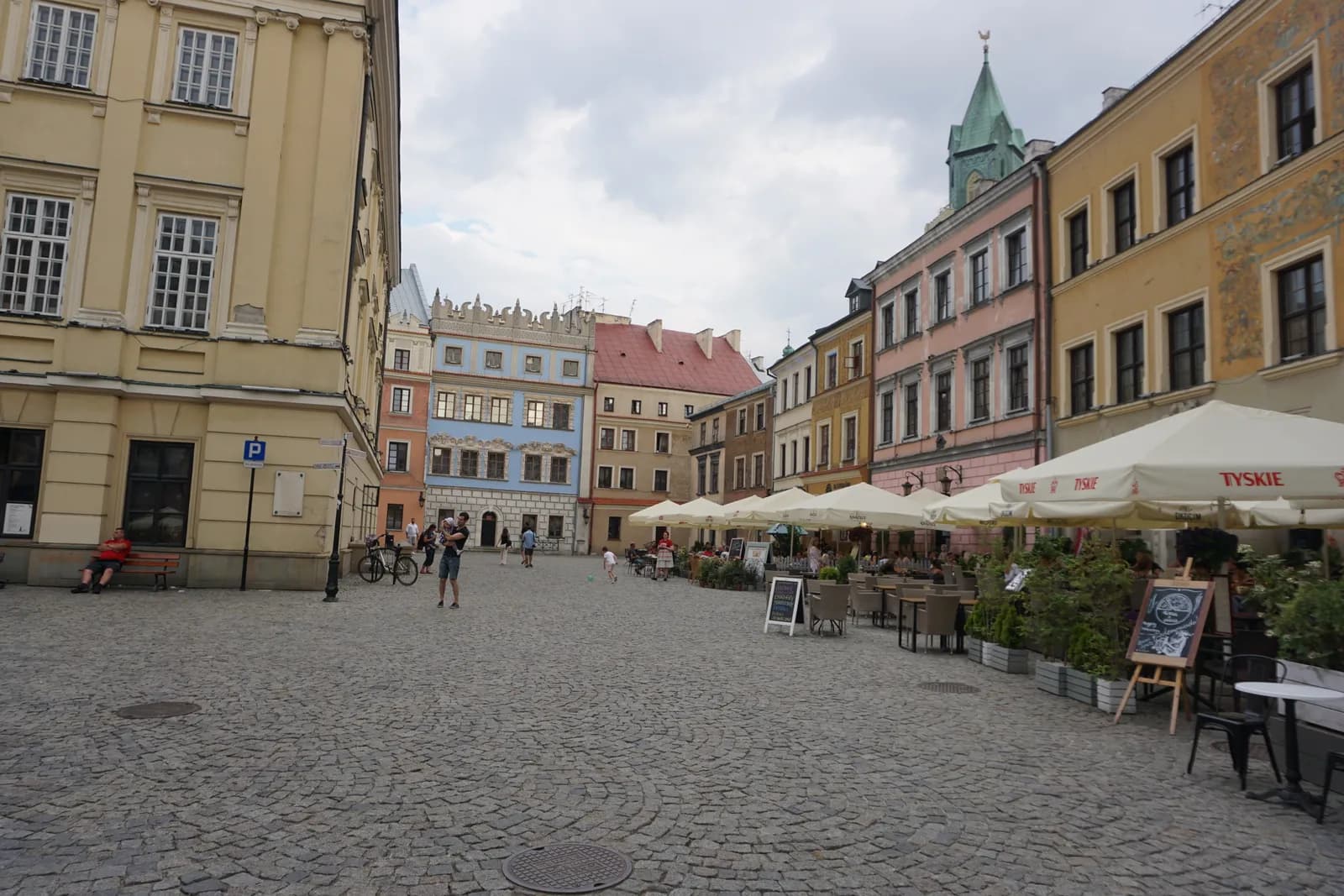 A cobblestone square in a European city, surrounded by colorful historic buildings and outdoor cafes with umbrellas.